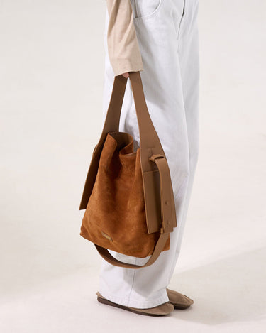 Medium Drippy Tote Bag in caramel suede with tan leather accents, worn on the shoulder by a person in white jeans.
