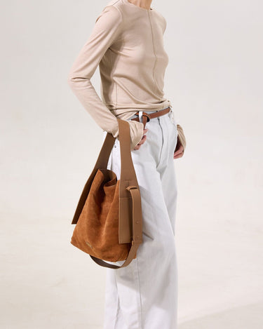 Medium Drippy Tote Bag in Caramel suede with leather straps. Model wears beige top and light jeans.
