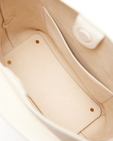 Beige vegan leather tote bag interior, showing main compartment and divider with brass studs.