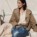 Medium Gather Bag Set in navy blue leather, featuring drawstring closure and adjustable straps. Model wearing tan jacket.