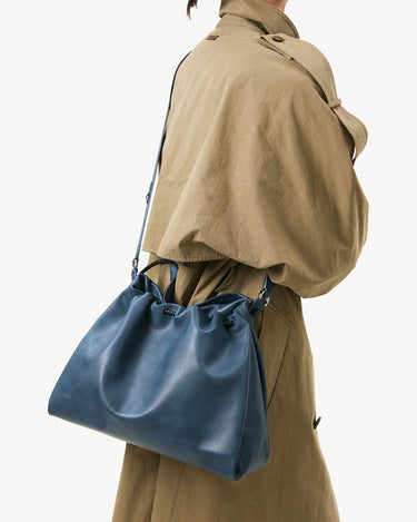 Medium Gather Bag Set in navy blue leather, worn by a person in a tan trench coat.