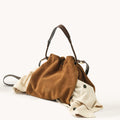 Ochre suede medium Gather Bag set with beige garment spilling out, showcasing its spacious design.