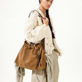 Medium Gather Bag Set in Ochre Suede with leather details, worn by a woman in a knit sweater and beige pants.