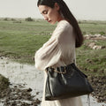 Woman in a flowing cream dress carrying an Onyx Medium Gather Bag with gold bead detail