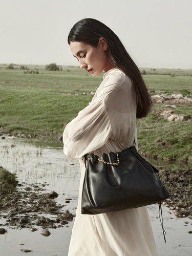 Woman in a flowing cream dress carrying an Onyx Medium Gather Bag with gold bead detail