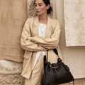 Woman in tan linen suit with black leather Medium Gather Bag, showcasing adjustable strap and drawstring closure.
