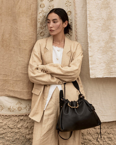 Woman in tan linen suit with black leather Medium Gather Bag, showcasing adjustable strap and drawstring closure.