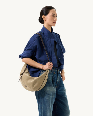 Large Luna Hobo Bag in Dune Suede with leather strap, styled by a woman in a blue shirt and jeans.
