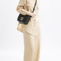 Black leather Medium Reset Tofu Bag with gold buckle, worn by a woman in tan linen outfit.