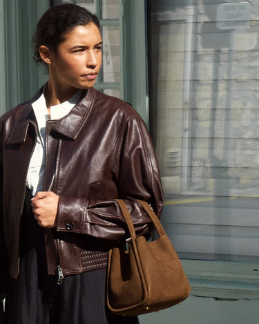 Medium Song Bag in Agarwood nubuck leather with gold hardware, carried by a woman in a brown leather jacket.