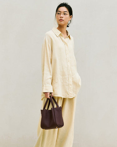 Medium Song Bag in burgundy full-grain leather with adjustable strap, carried by a woman in light yellow attire.
