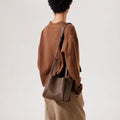 Medium Song Bag in chocolate pebbled leather with gold hardware, worn on shoulder by a person in brown sweater.