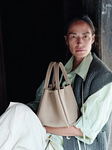 Medium Song Bag in Cream Apricot leather, held by a woman in casual attire.