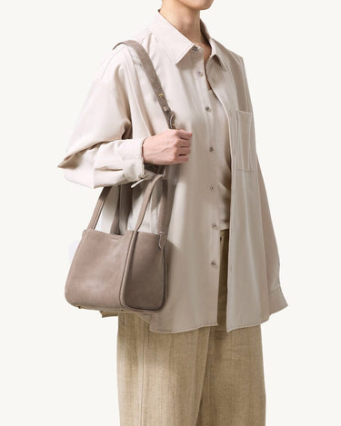 Medium Song Bag in Haze nubuck leather, worn on shoulder by a person in neutral-toned clothing.