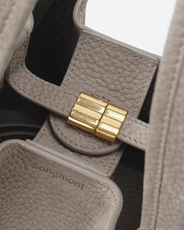Medium Song Bag in Haze nubuck leather with gold magnetic clasp and embossed Songmont logo.