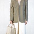Model wearing an oversized taupe blazer and cream trousers, holding an ivory pebble-grain leather Medium Song Bag.