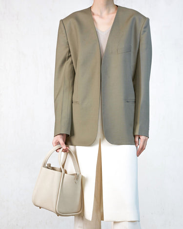 Model wearing an oversized taupe blazer and cream trousers, holding an ivory pebble-grain leather Medium Song Bag.