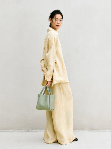 Medium Song Bag in Jade, a textured green leather handbag with double straps, held by a woman in linen attire.