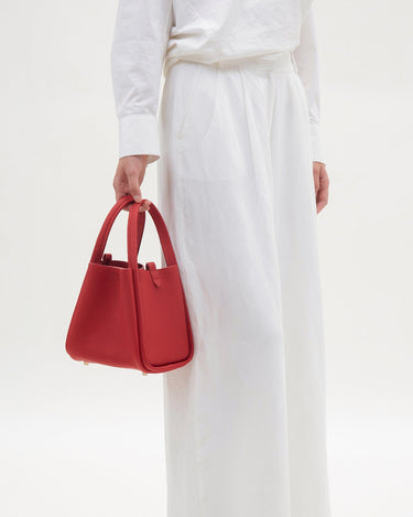 Medium Song Bag in Lucky Red pebbled leather with twin top handles and metallic base studs.