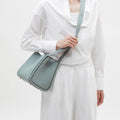 Pale blue full-grain leather Medium Song Bag with adjustable strap worn by a person in white clothing.