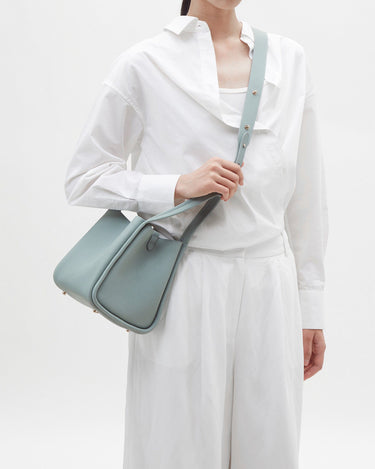 Pale blue full-grain leather Medium Song Bag with adjustable strap worn by a person in white clothing.