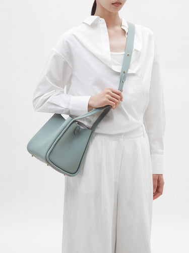 Pale blue full-grain leather Medium Song Bag with adjustable strap worn by a person in white clothing.