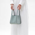 Light blue full-grain leather medium song bag with a textured finish, dual top handles, and four protective metal feet.