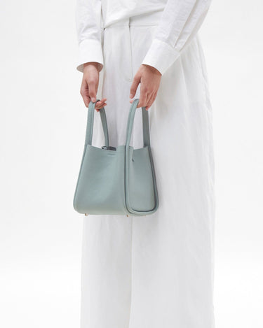 Light blue full-grain leather medium song bag with a textured finish, dual top handles, and four protective metal feet.