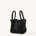 Medium Song Bag in black full-grain leather with dual top handles and protective metal feet.
