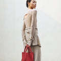 Medium Song Bag in Poppy red nubuck leather, held by a woman in a tan knit outfit.