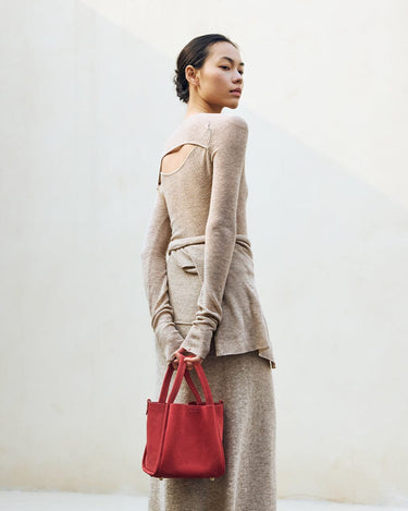 Medium Song Bag in Poppy red nubuck leather, held by a woman in a tan knit outfit.