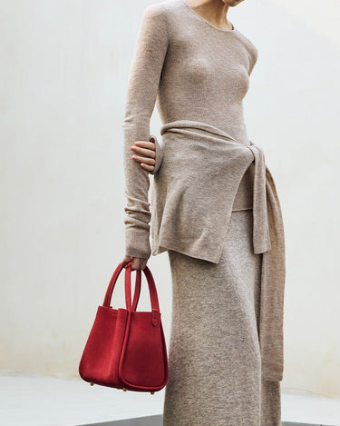 Medium Song Bag in poppy red nubuck, structured tote with dual handles and gold feet, worn with neutral knit.