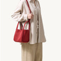 Red medium Song bag carried by a woman wearing a beige oversized shirt and linen pants.