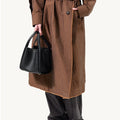 Medium Song Bag in black vegan leather, held by a model wearing a brown coat and black pants.