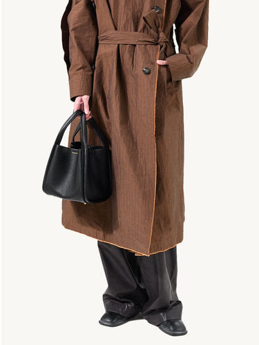 Medium Song Bag in black vegan leather, held by a model wearing a brown coat and black pants.