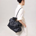 Medium Yore Duffle Bag in black vegetable-tanned leather with white stitching and gold hardware, worn by a woman.