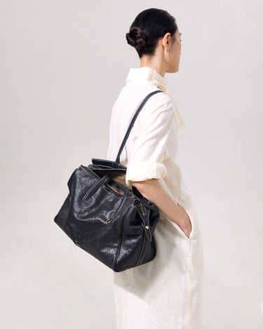 Medium Yore Duffle Bag in black vegetable-tanned leather with white stitching and gold hardware, worn by a woman.