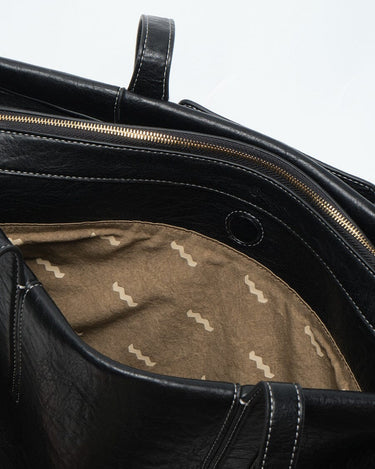 Medium Yore Duffle Bag in Onyx, black vegan leather with white stitching and wave-patterned tan lining. Features gold zipper.