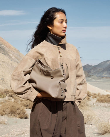 Medium Yore Hobo Bag in Cobble Grain leather, worn by a woman in a suede jacket in a desert landscape.