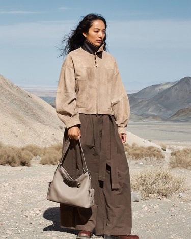 Medium Yore Hobo Bag, cobble grain leather, light grey. Styled with tan jacket and brown skirt in a desert landscape.