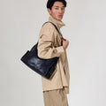 Medium Yore Hobo Bag in Onyx, worn by a man in tan clothing. Textured leather bag.