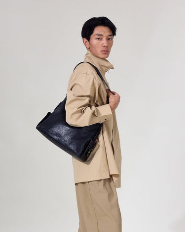 Medium Yore Hobo Bag in Onyx, worn by a man in tan clothing. Textured leather bag.