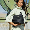 Medium Yore Hobo Bag in black pebble-grain leather held by a woman in a light green outfit.