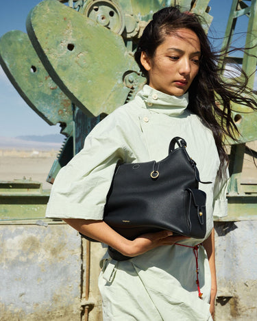 Medium Yore Hobo Bag in black pebble-grain leather held by a woman in a light green outfit.