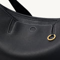 Black pebbled leather hobo bag with white stitching and a gold ring detail.