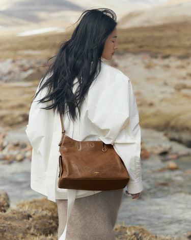 Medium Yore Hobo Bag in Sandal color, made of vegetable-tanned leather, worn by a woman outdoors.