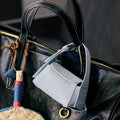 Sky Mini Drippy AirPods Case made of pebbled leather with stainless steel hardware, attached to a large black leather bag.