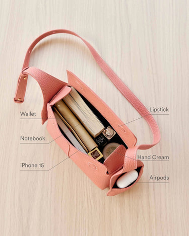 Open pink Mini Drippy Roof Bag showcasing organized contents: iPhone 15, notebook, wallet, lipstick, hand cream, and AirPods.