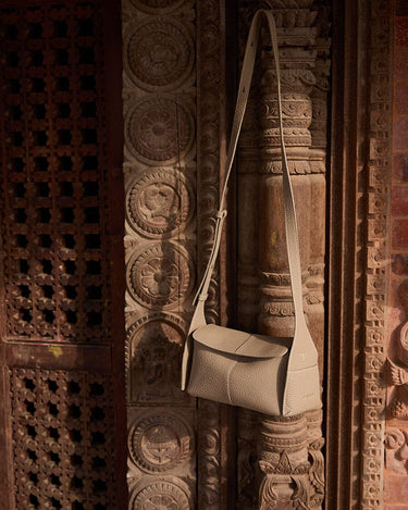 Cobble pebble leather Mini Drippy Roof Bag, structured crossbody with flap closure, against carved wood.