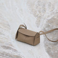 Mini Drippy Roof Bag in Cobble textured leather, with a flap closure and adjustable strap, resting on a marble-like surface.